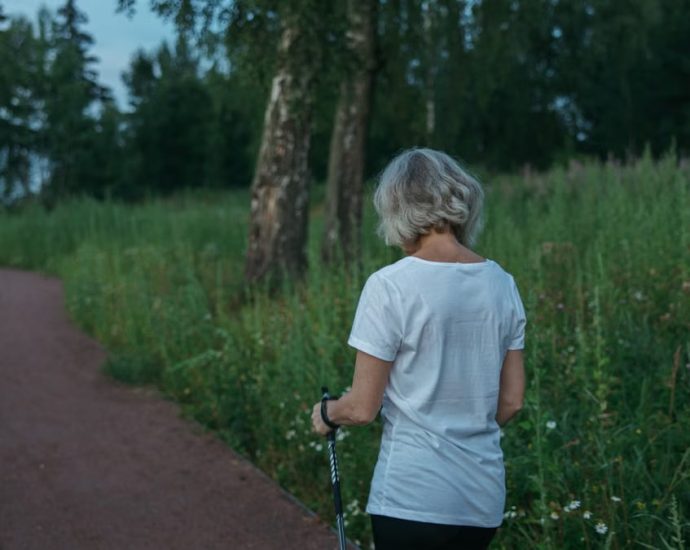 Elderly woman practicing Nordic walking on a park trail, promoting health and fitness.