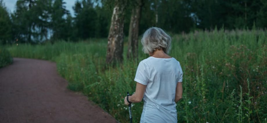 Elderly woman practicing Nordic walking on a park trail, promoting health and fitness.